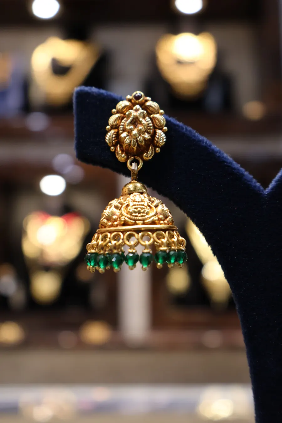A gold jhumka earring with bead drops on a velvet stand