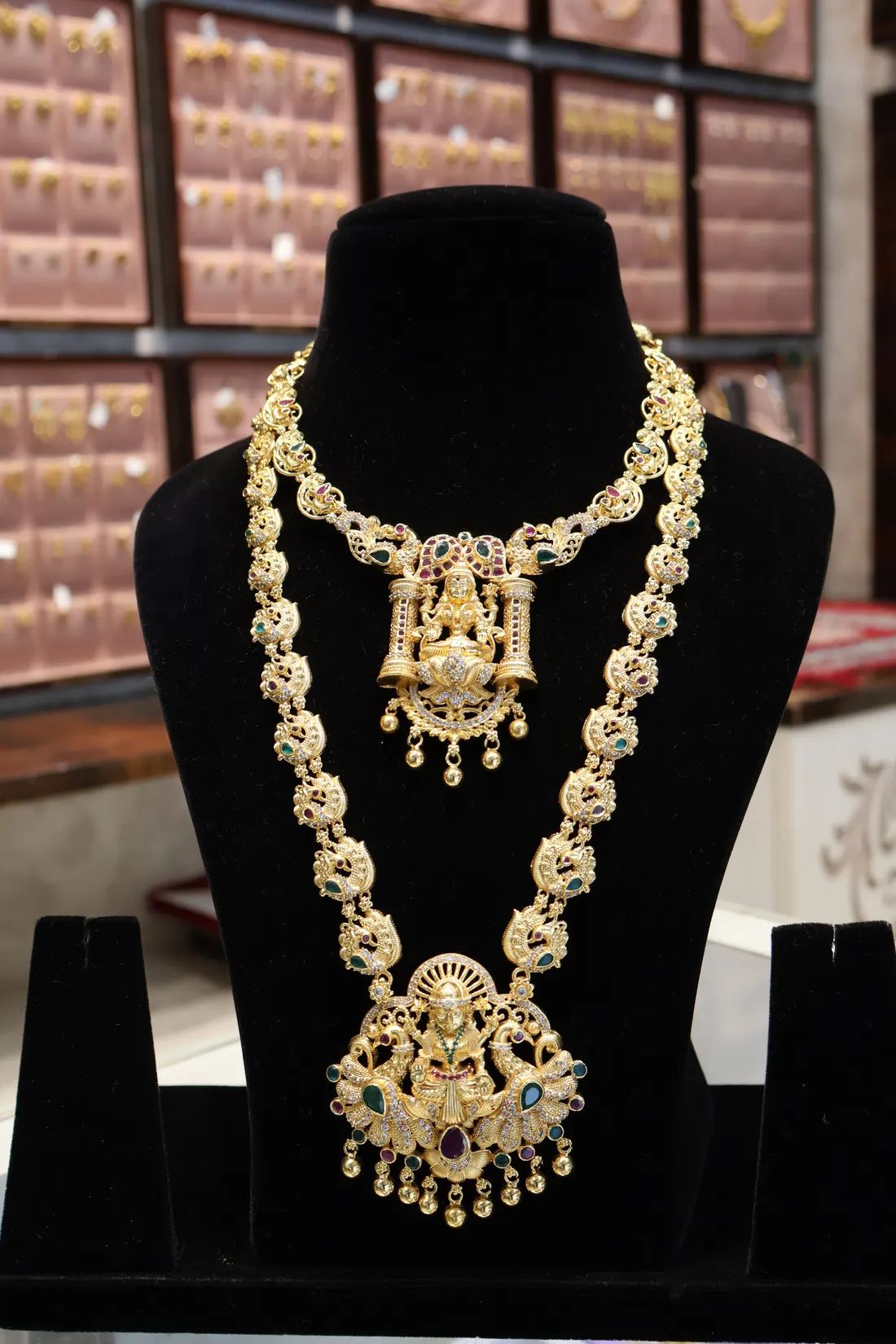 A long haram and a shorter necklace with Lakshmi pendants, made as a set, on a black bust