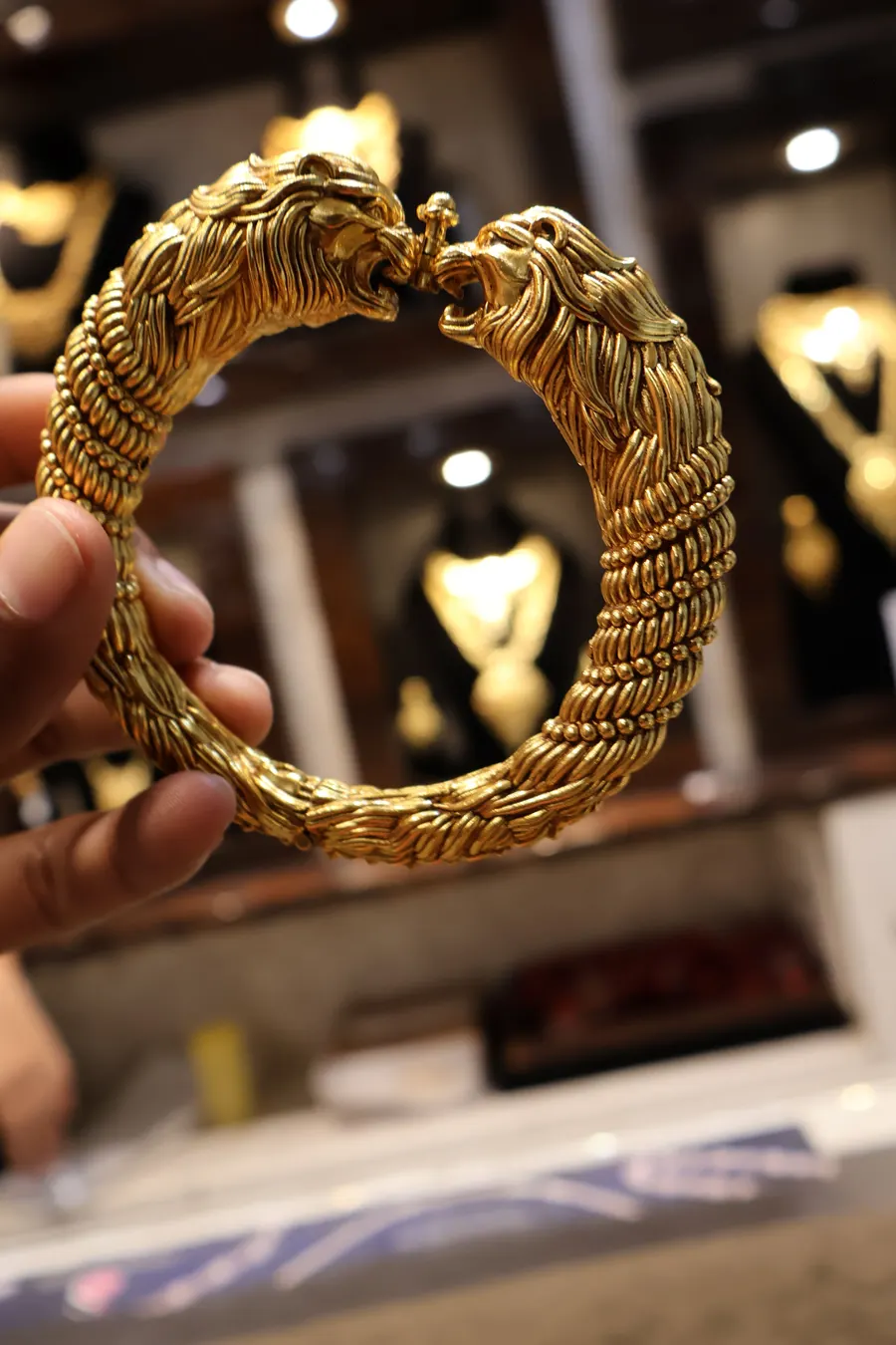 A lion-head gold kada held in a hand