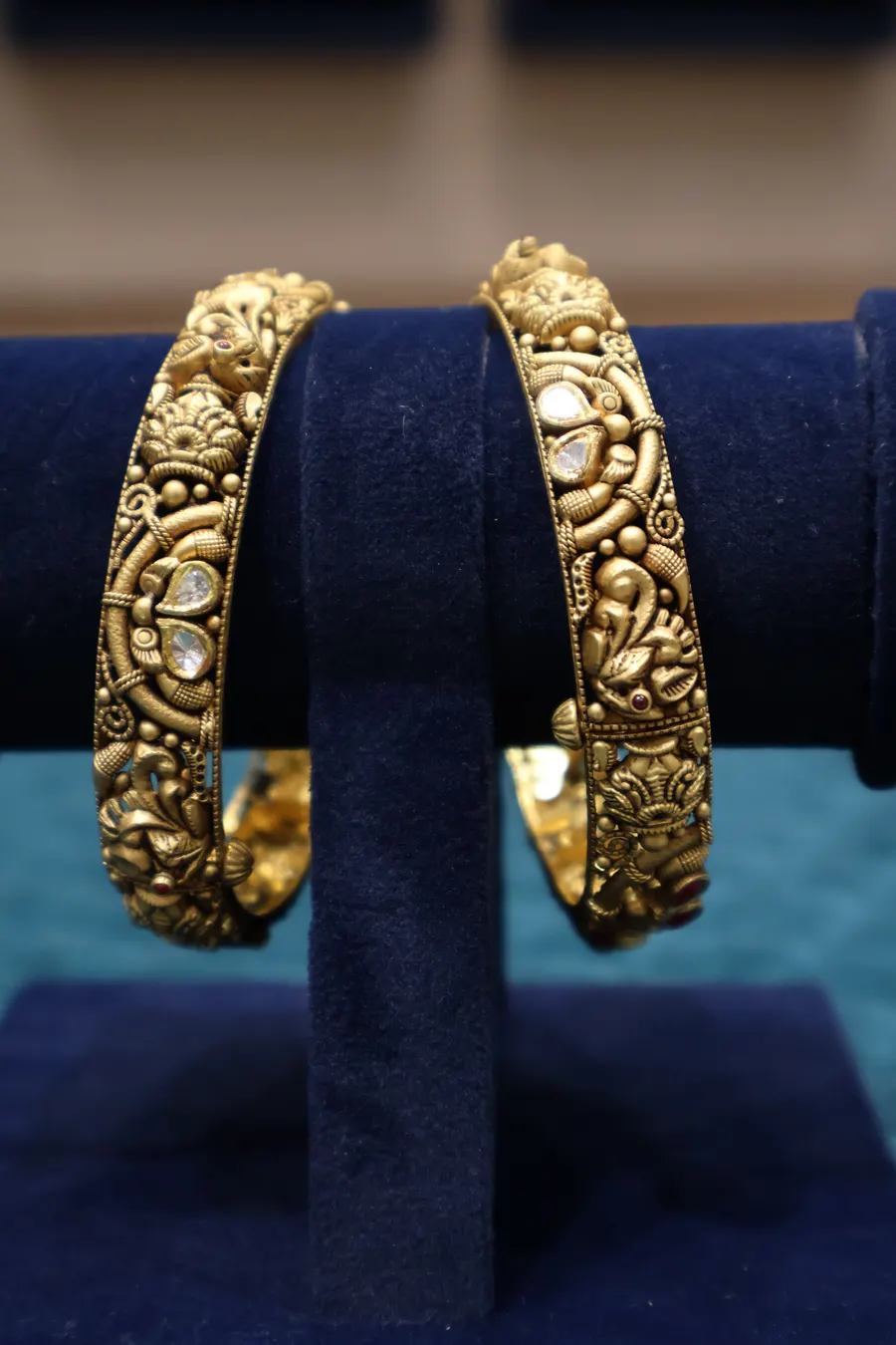 A pair of carved gold kadas on a blue velvet stand