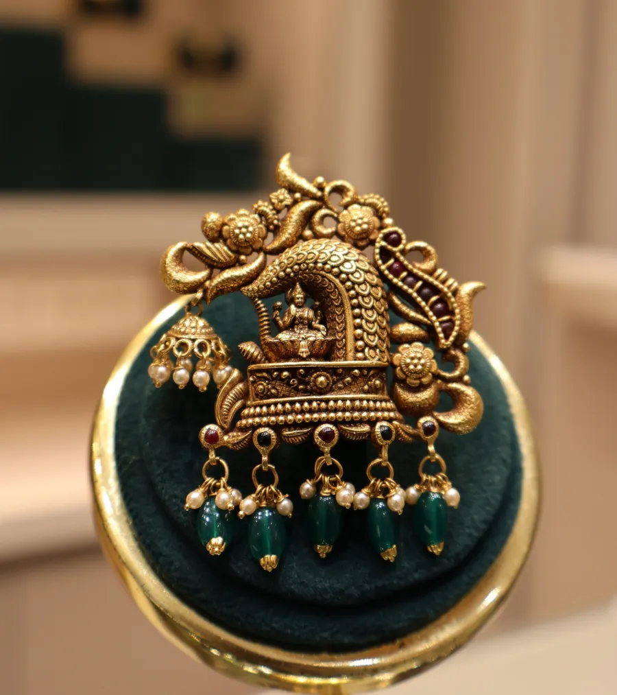 A temple pendant with green bead drops on a velvet stand