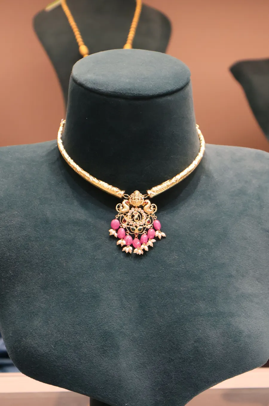 A slim gold necklace with a pink stone pendant on a bust