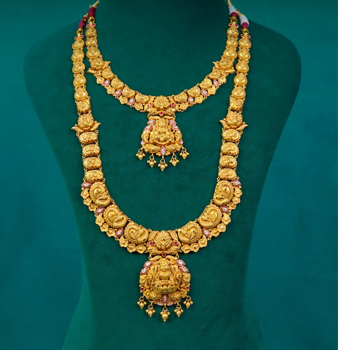 A haram and a shorter necklace with Lakshmi pendants, worn as a pair, on teal velvet