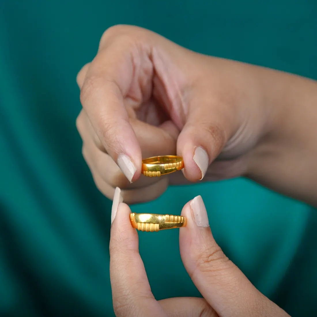 Two plain gold bands held between finger and thumb, on teal