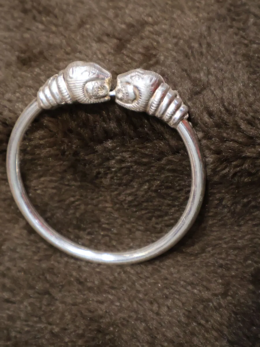 A silver kada with two carved heads at its ends