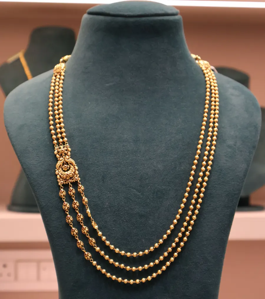 A three-strand gold bead chain on a velvet bust